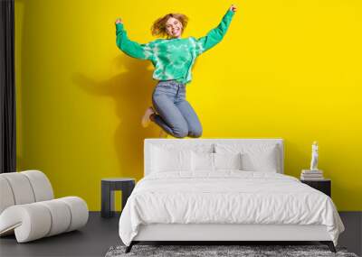 Full length photo of lucky positive woman wear green sweatshirt jumping high rising fists empty space isolated yellow color background Wall mural