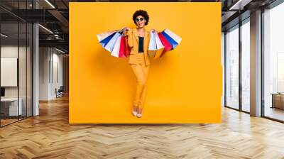 Full length photo of positive bruntte hair dark skin girl feel enthusiastic hold bags addicted shopper shopping on leisure time wear style outfit sunglass high-heels isolated yellow color background Wall mural