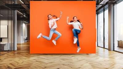 Full length photo of positive rejoicing two girlfriends jump rest relax win school sport competition raise fists wear white shirt denim jeans isolated over orange color background Wall mural