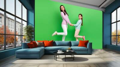 Full length photo of pretty excited little girl mom dressed casual clothes dancing holding arms isolated green color background Wall mural