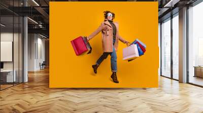 Full length photo of pretty lady jumping walk shopping center carry many packs wear casual pink coat pullover jeans leopard print shoes isolated yellow color background Wall mural