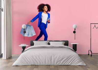 Full length photo of pretty woman wear blue jacket hold shopping bags smartphone look go empty space isolated on pink color background Wall mural