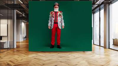 Full length photo of serious old cool man posing model wear decor balls baubles on jacket sunglass hat isolated on green color background Wall mural