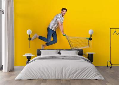 Full length photo of shiny impressed man wear white t-shirt jumping high buying supermarket food isolated yellow color background Wall mural