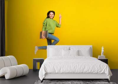 Full length photo of young cheerful girl hold laptop show fingers peace v-symbol isolated over yellow color background Wall mural