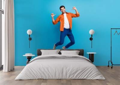 Full length portrait of crazy carefree active man jumping point fingers self himself isolated on blue color background Wall mural