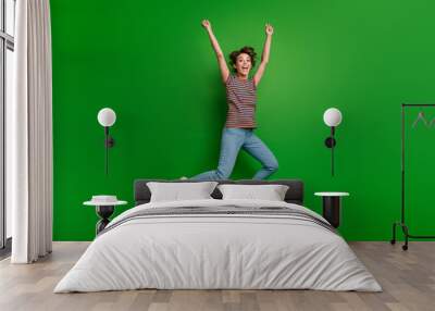 Full length portrait of delighted carefree person jumping raise fists achievement empty space isolated on green color background Wall mural