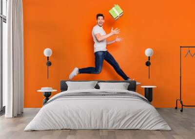 Full length profile photo of crazy guy jump high up catch big green giftbox unexpected present wear striped t-shirt jeans shoes isolated bright orange color background Wall mural