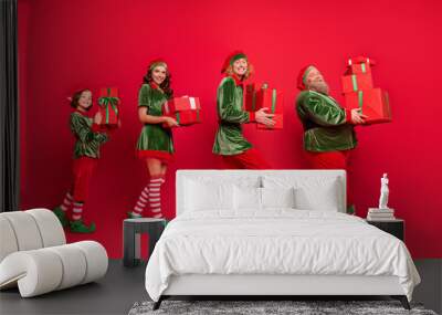 Full length profile photo of line santa service different high hold giftboxes wear holiday costumes isolated on red background Wall mural