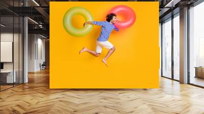 Full length profile side photo of guy jump run hold two rubber buoys wear blue white shorts isolated on yellow color background Wall mural