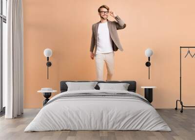 Full size photo of attractive dreamy young man walk look empty space smile isolated on beige color background Wall mural