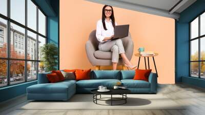 Full size photo of cheerful data analytic worker young lady sit chair with netbook remote communicating isolated on beige color background Wall mural