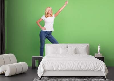 Full size photo of cool blond aged lady point empty space wear white t-shirt jeans isolated on green color background Wall mural