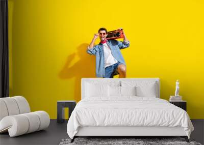 Full size photo of cool guy wear jeans jacket shorts touch sunglass hold boombox at summer party isolated on yellow color background Wall mural