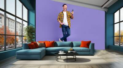 Full size photo of cool man wear yellow plaid shirt jeans pants look at smartphone arm in pocket isolated on purple color background Wall mural