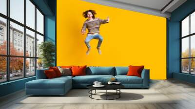 Full size photo of eccentric guy dressed ornament sweater jeans jumping near offer empty space isolated on yellow color background Wall mural