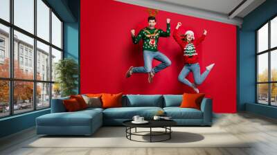 Full size photo of funky lady and guy jumping excited by x-mas prices wear ugly ornament jumpers and headwear isolated red color background Wall mural