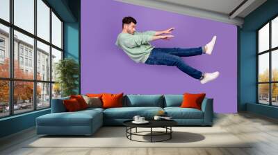 Full size photo of handsome young man flying away strong wind blow push dressed stylish khaki clothes isolated on purple color background Wall mural