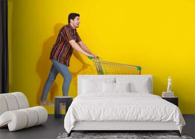 Full size photo of nice young man push trolley empty space wear shirt isolated on yellow color background Wall mural