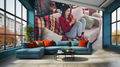 Full size photo of positive girl chat on smartphone sit couch wear red jumper in house indoors with x-mas christmas noel ornament Wall mural