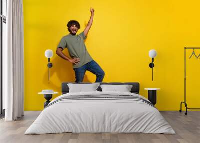 Full size photo of positive guy dressed khaki t-shirt jeans stand near empty space raising finger up isolated on yellow color background Wall mural