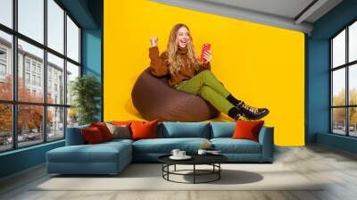 Full size photo of pretty young woman use smart phone raise fist isolated on yellow color background Wall mural