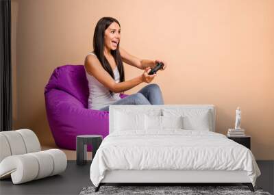 Full size profile photo of optimistic brunette girl sit pouf with playstation wear top jeans isolated on beige background Wall mural