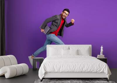 Full size profile photo of optimistic nice brown hair man jump with laptop wear spectacles sweater isolated on purple background Wall mural