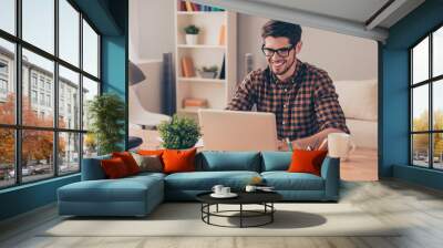 Handsome cheerful young man in glasses typing on laptop Wall mural