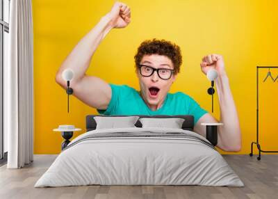 Handsome curly-haired shocked young guy wearing casual green t-shirt and glasses, showing surprised gesture. Isolated over yellow background Wall mural