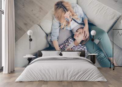 Hih angle above view photo of charming blond mommy daughter two ladies relaxing lying comfy couch hold arms overjoyed stay home quarantine time spend weekend together living room indoors Wall mural