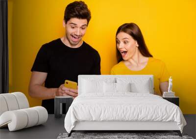 Look. Photo of two crazy students people guy lady holding telephones reading good news influencer blog open mouth wear casual black t-shirts isolated yellow color background Wall mural