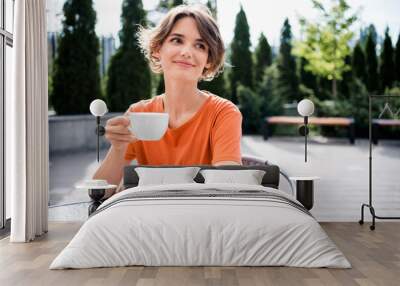 Photo of adorable dreamy lady wear orange t-shirt sitting cafeteria drinking hot tea outside urban city street Wall mural