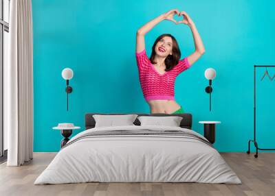 Photo of adorable girlish woman with straight hairdo dressed knitwear top look at heart symbol over head isolated on blue color background Wall mural