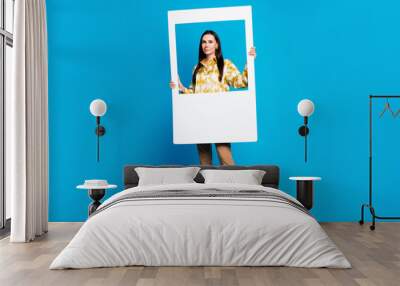 Photo of adorable lovely woman wear trendy clothes hold frame isolated on blue color background Wall mural