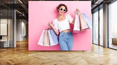 Photo of adorable nice satisfied girl wear white top denim jeans toothy beaming hold bags new clothes isolated on pink color background Wall mural