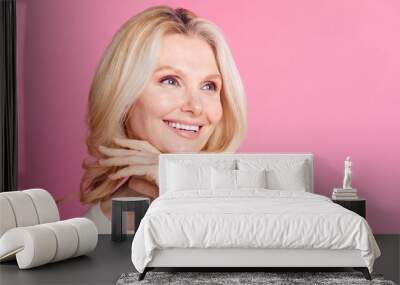 Photo of adorable senior woman in stylish clothes look empty space isolated on pink color background Wall mural