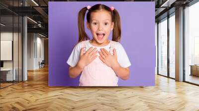 Photo of amazed cute little girl gesture show ask me wear pink overall dress isolated on violet color background Wall mural