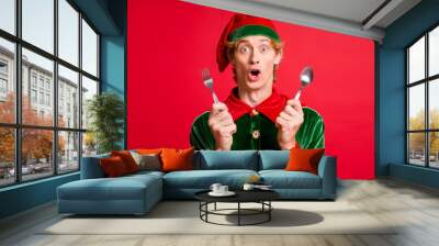 Photo of amazed elf guy hold spoon fork x-mas christmas party feast concept isolated over red shine color background Wall mural