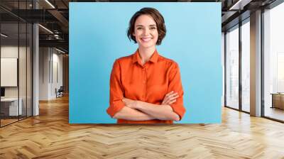 Photo of attractive bossy lady bobbed hairdo arms crossed self-confident person worker friendly smile white teeth good mood wear orange office shirt isolated blue color background Wall mural