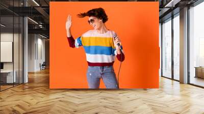 Photo of attractive carefree person arm hold mic look empty space palm wave isolated on orange color background Wall mural