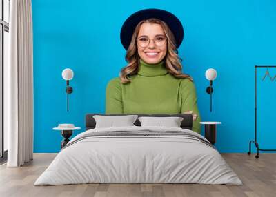 Photo of attractive cheerful lady youngster hold arms crossed self-confident person wear specs retro hat casual green turtleneck isolated blue color background Wall mural