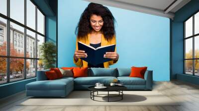 Photo of attractive dark skin wavy lady holding corporate business knowledge book swallow useful information wear specs stylish yellow suit blazer isolated blue color background Wall mural