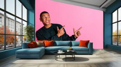 Photo of attractive funny guy wear sweatshirt showing two fingers emtpy space isolated pink color background Wall mural