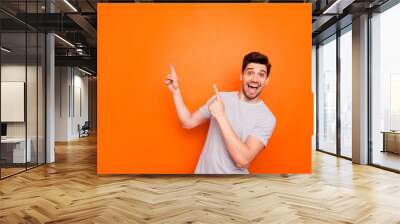 Photo of attractive guy hold hands fingers direct up empty space excited good mood sales person wear striped t-shirt isolated bright orange color background Wall mural