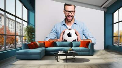 Photo of attractive handsome guy holding leather white black soccer ball yelling loud supporting team football match wear specs casual denim outfit isolated grey color background Wall mural