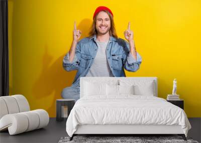 Photo of attractive positive man wear denim jacket pointing two fingers up emtpy space isolated yellow color background Wall mural