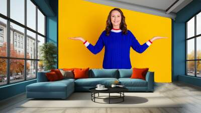 Photo of attractive retired woman compare hold empty space dressed stylish blue knitted clothes isolated on yellow color background Wall mural