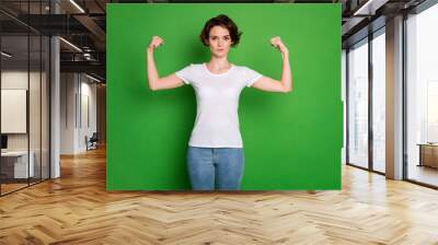 Photo of attractive self-confident lady wavy bobbed hairdo demonstrating two perfect shape biceps can beat any guy wear casual white t-shirt blue jeans isolated green color background Wall mural