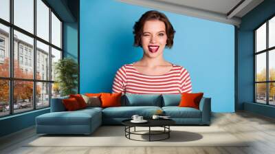 Photo of beautiful pretty cheerful lady playful coquettish person sticking tongue out mouth blinking eye wear casual red white shirt isolated bright blue color background Wall mural